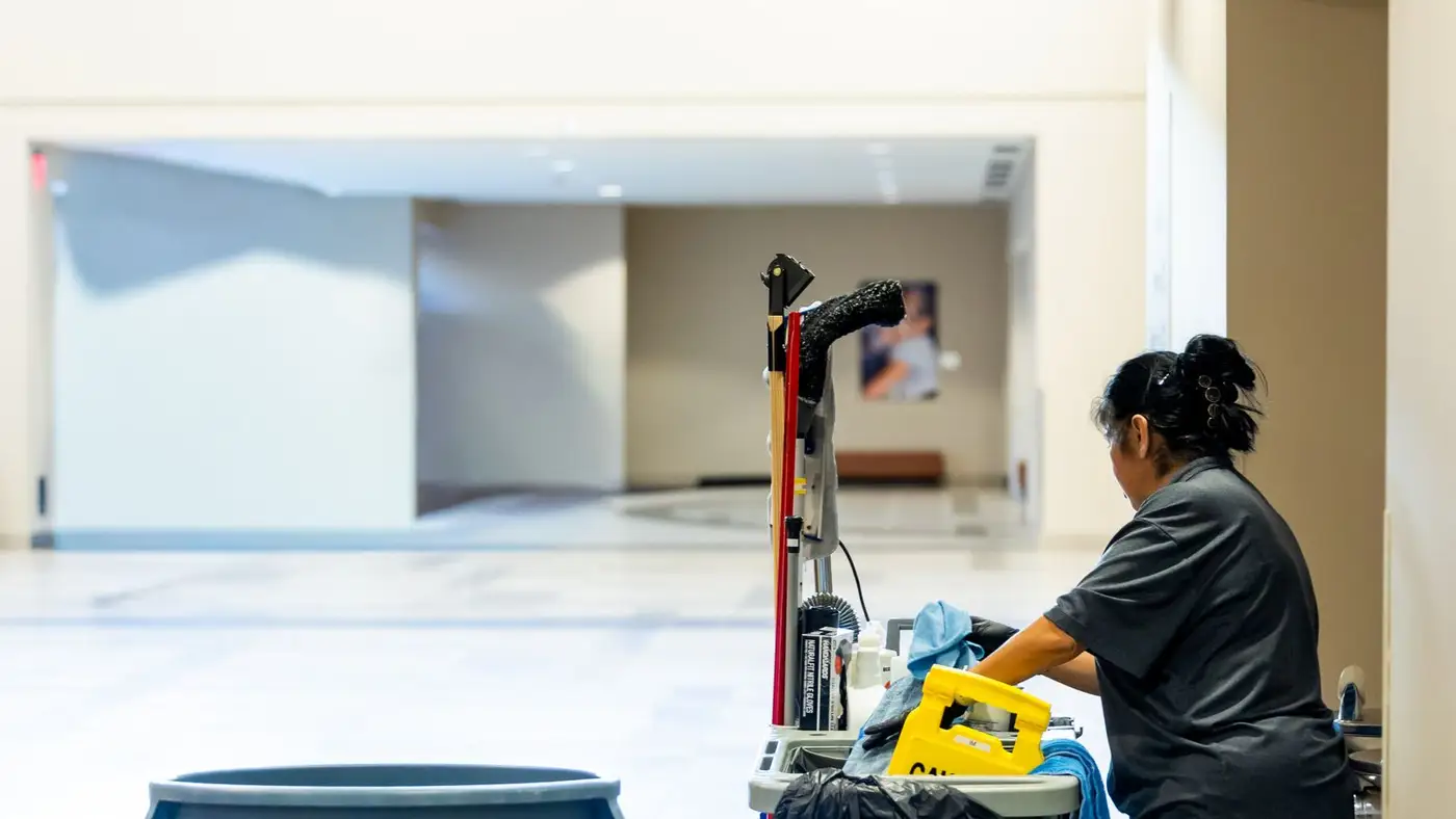 Janitorial worker with a cleaning cart in a commercial hallway